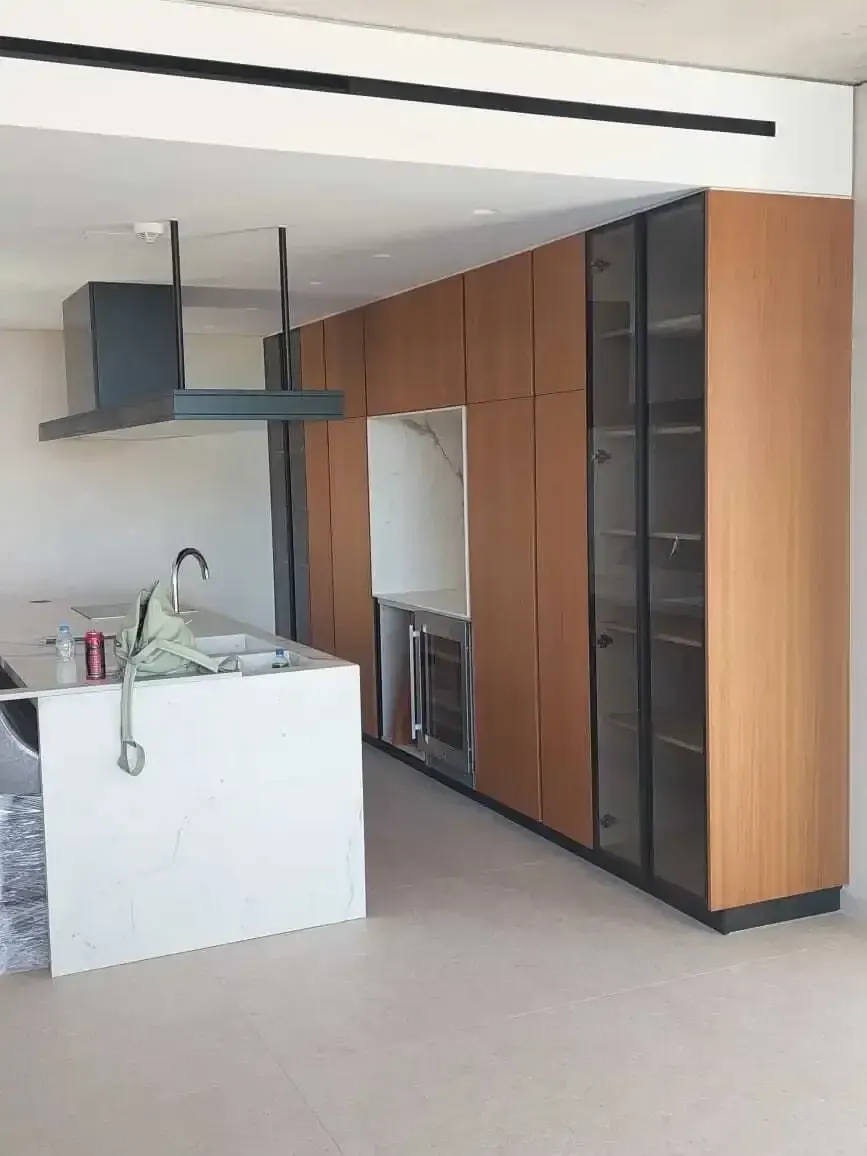 Wood-finish tall kitchen units with a white stone island and a suspended black extractor