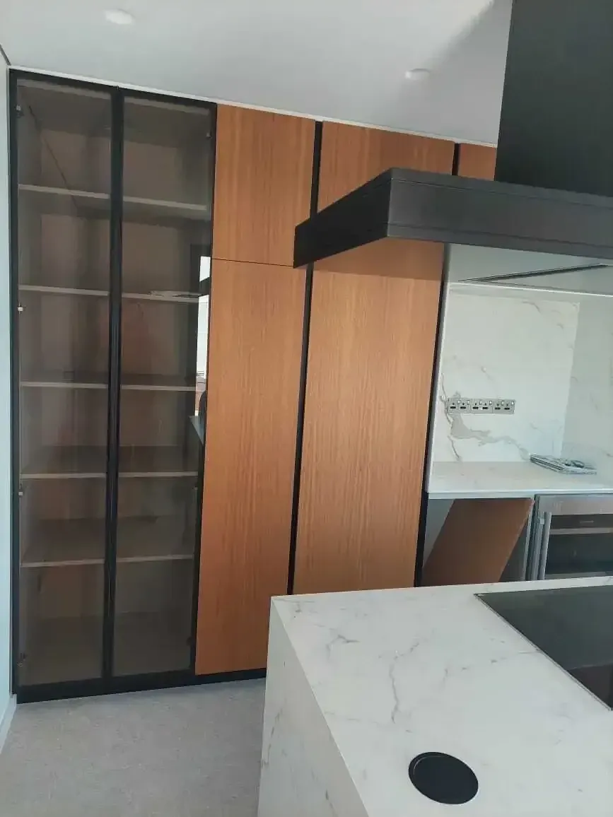 Floor-to-ceiling smoked glass display cabinet with black frames next to the wood units
