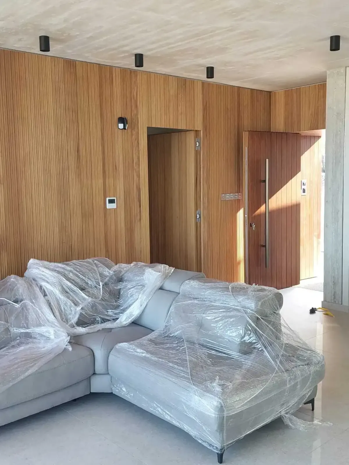 Living room with wood-clad walls, the hidden door and the main entrance
