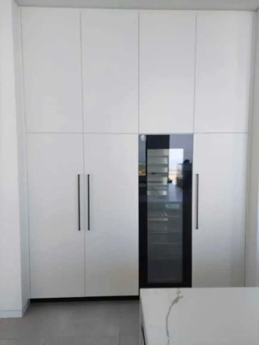White tall units with long black handles and a built-in wine fridge