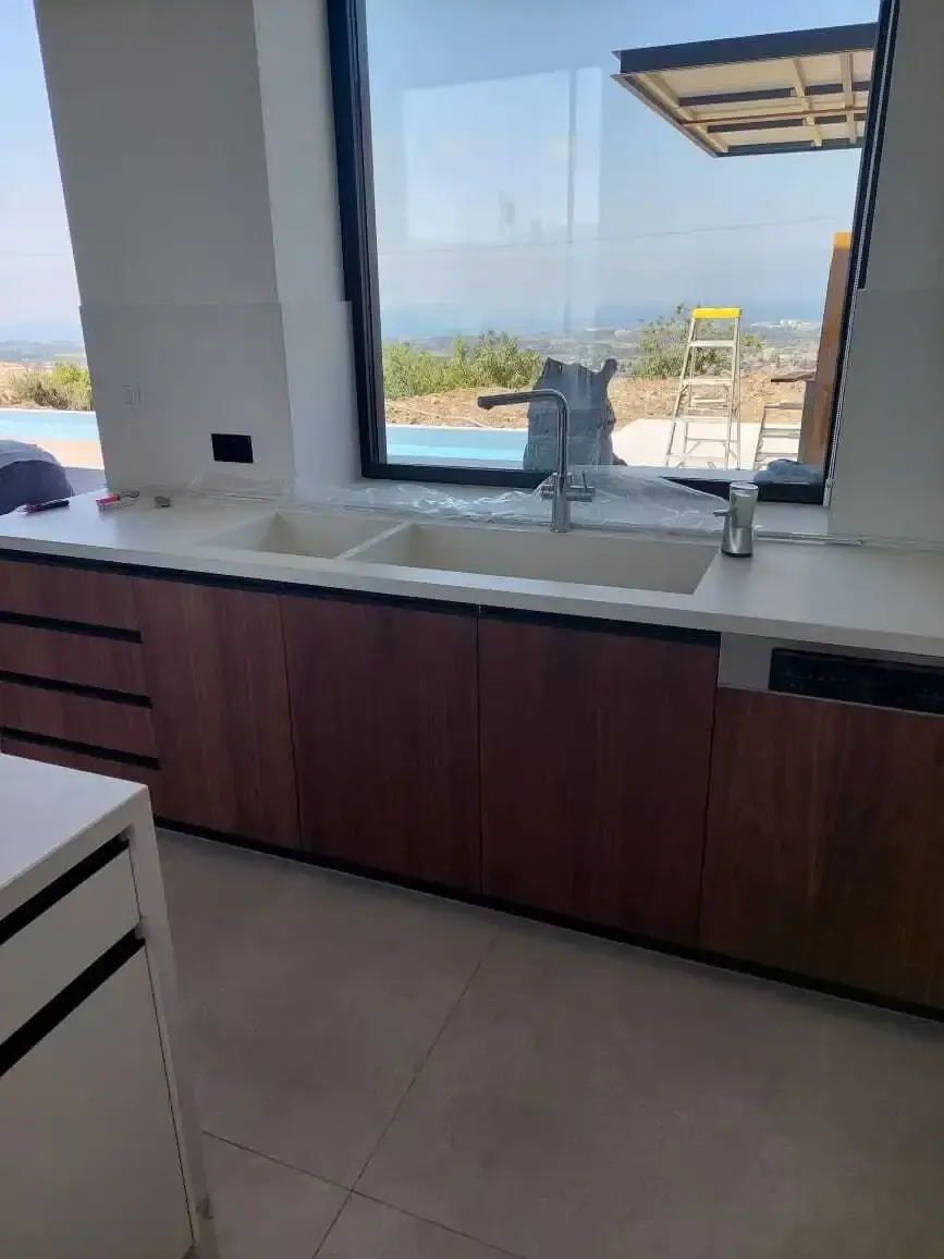 Undermount sink set into the white worktop above walnut units, with a sea view