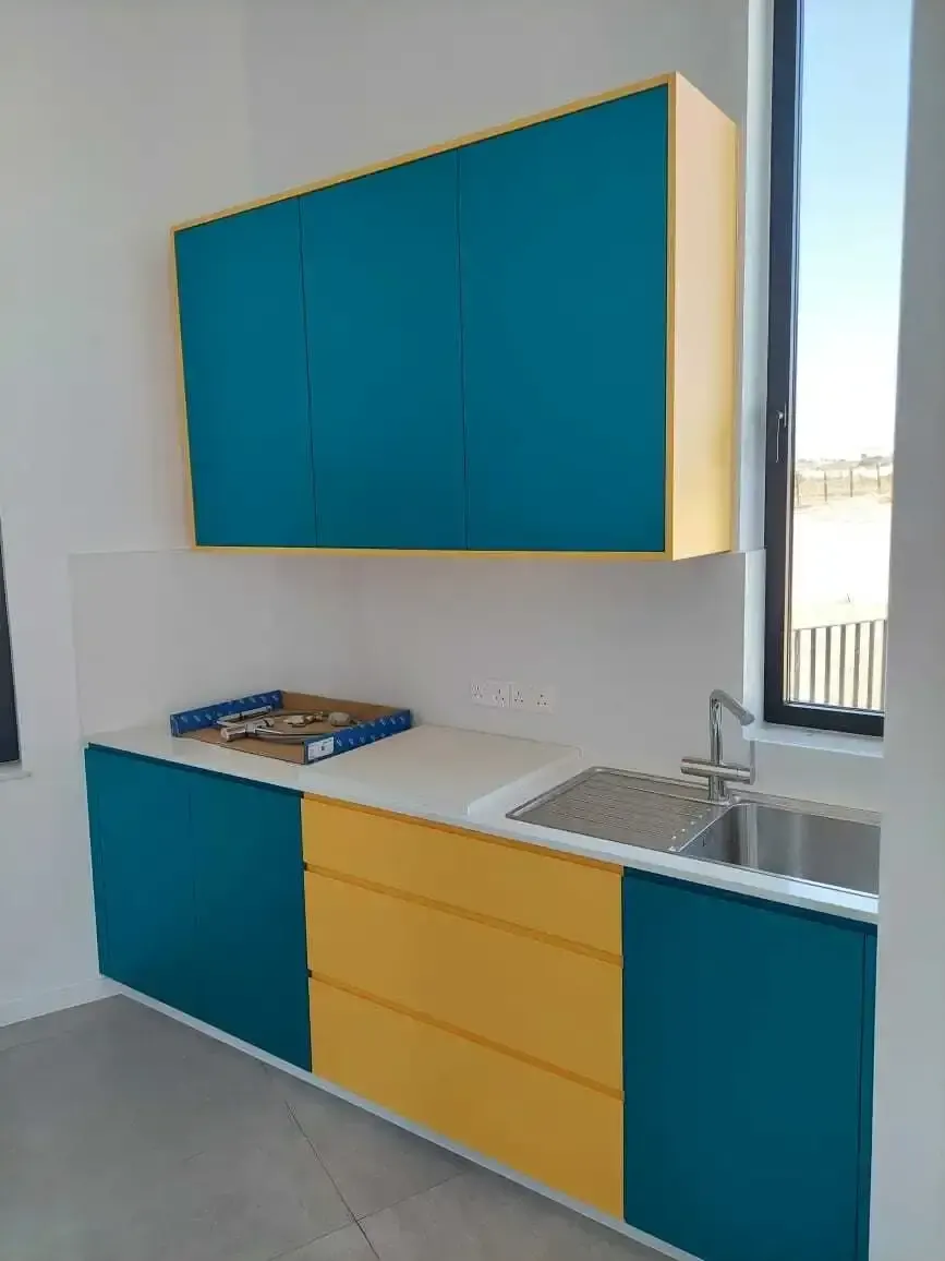 Compact kitchen with teal base and wall units and a bank of yellow drawers