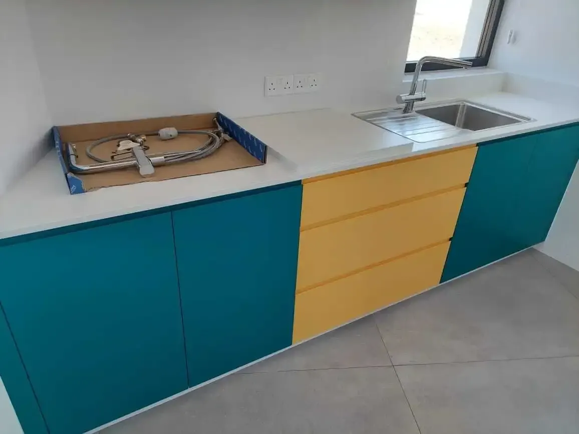 Teal and yellow units with the sink and white worktop during installation