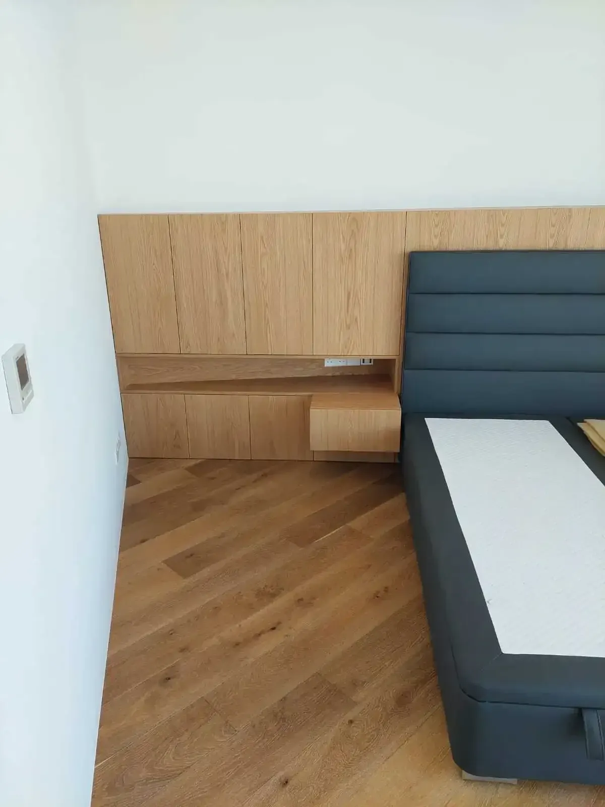 Oak headboard wall panelling with an integrated floating nightstand beside an upholstered bed