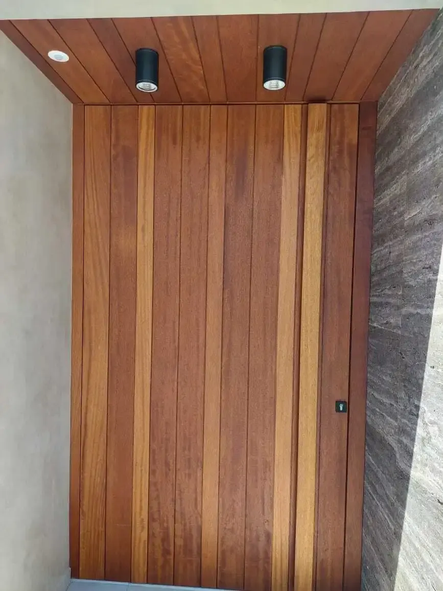 Full-height front door in vertical hardwood boards under a matching timber soffit with downlights